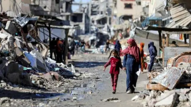 Palestinians walk past the ruins of houses destroyed in Gaza City, 20 March, 2024