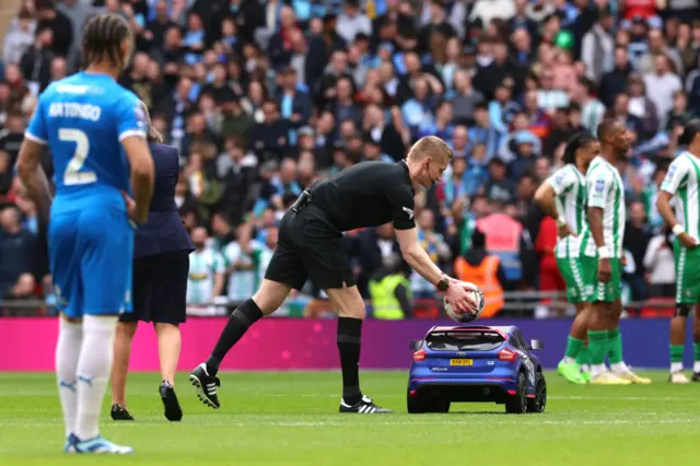 Referee Scott Oldham picks up the match ball from a remote controlled car