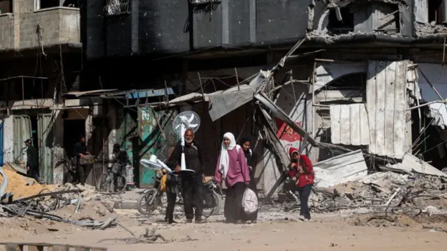 Palestinians carrying their belongings walk past damaged buildings in Khan Yunis on April 7, 2024