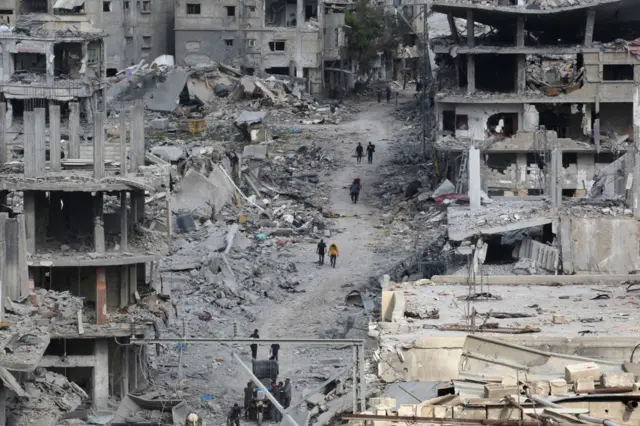 People walk among damaged buildings in Khan Younis, 8 April