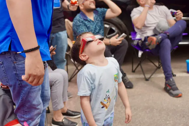 A child wearing solar glasses stares at the sky