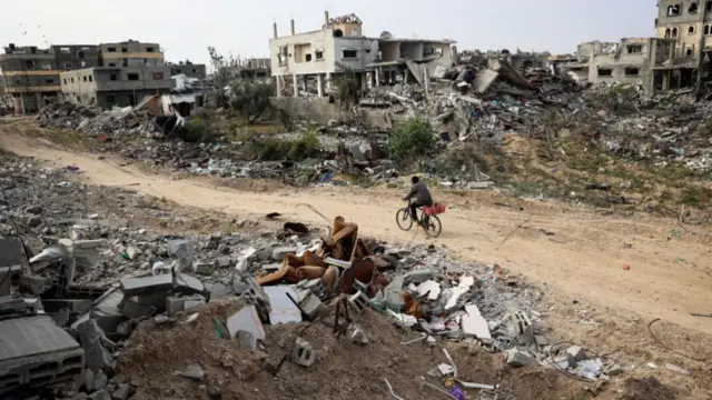 A Palestinian rides a bicycle past damaged buildings in Khan Yunis on April 8, 2024