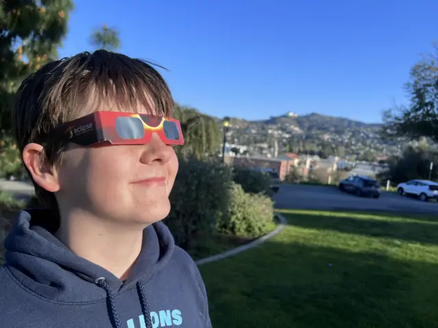 A boy is wearing solar eclipse viewing glasses