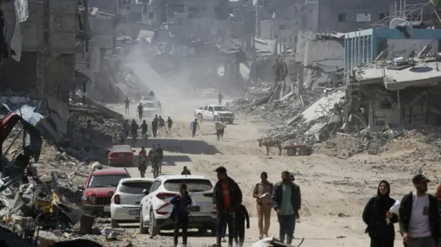 Palestinians walk amid destroyed buildings in the city of Khan Younis