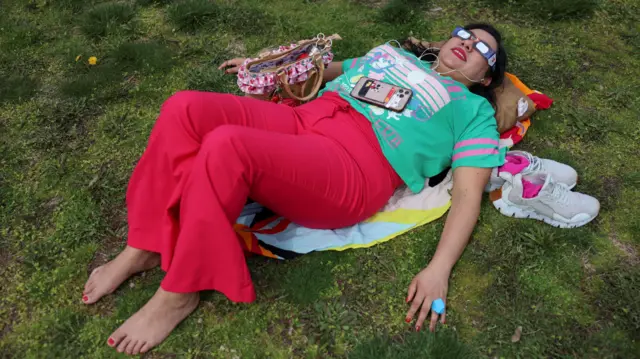 A woman lies on the grass viewing a partial solar eclipse at New York Hall of Science in Queens borough, New York City