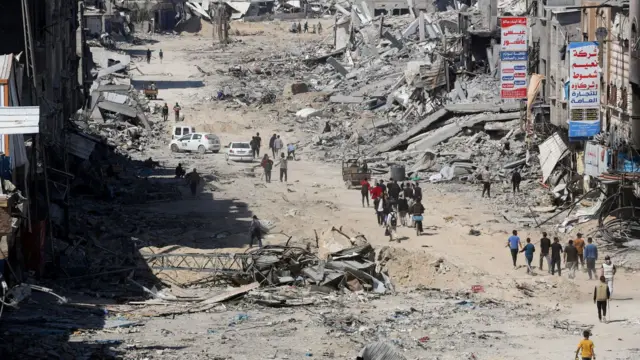 Groups of Palestinians returning to Khan Younis, with rubble piled high at the side of a road