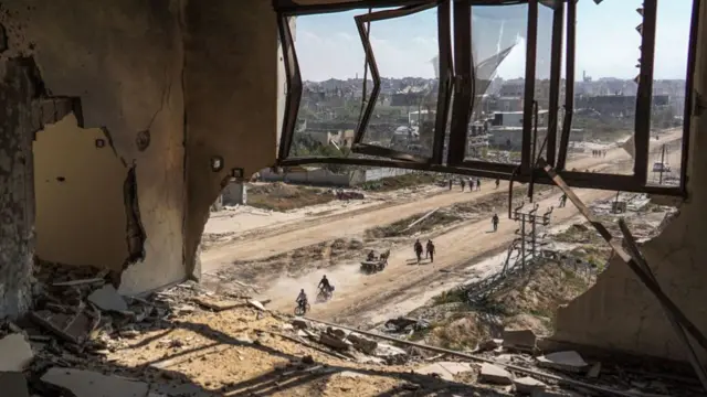 Palestinians walking along a damaged road photographed from inside a damaged building