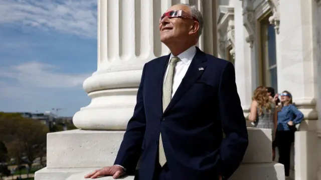 US Senate Majority Leader Chuck Schumer uses eclipse viewing glasses to look up at the partial solar eclipse