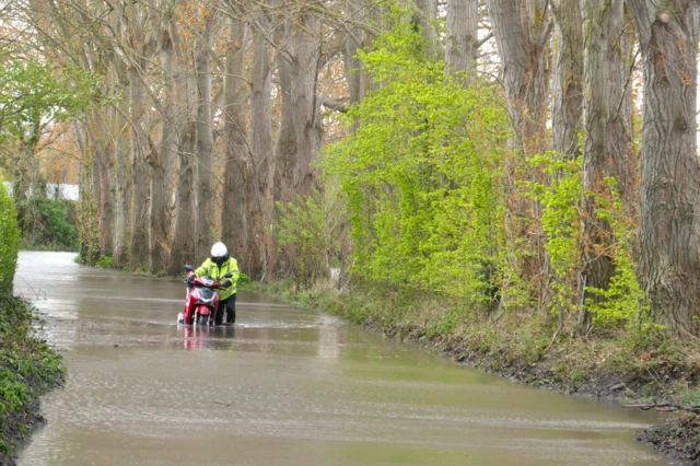 A moped rider drags the vehicle through flood water