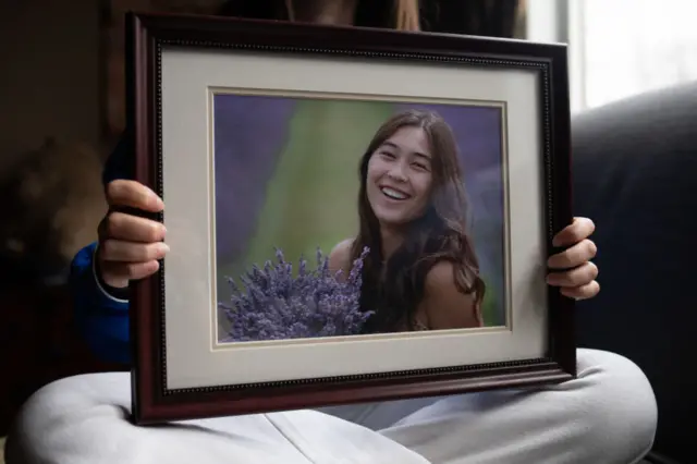 Reina St. Juliana, 16, holds a picture of her sister Hana St. Juliana at the St. Julianas home in Ortonville, Michigan on March 25, 2022.