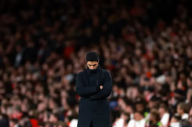 Arteta stands with his arms crossed and head down in thought