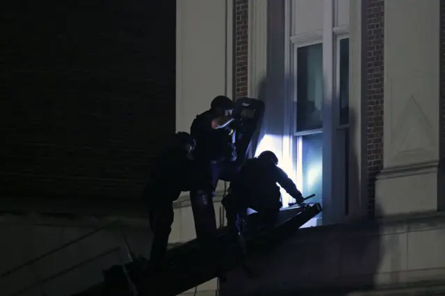 Police crouch near a window on a platform to enter the hall