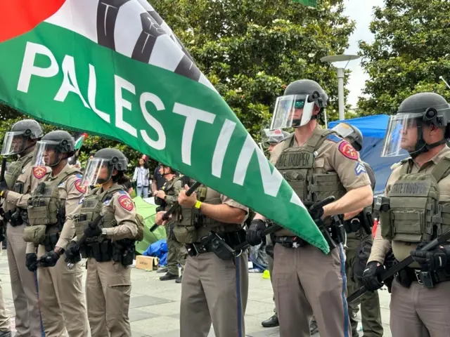 State troopers hold batons in their hands as a Palestinian flag waves