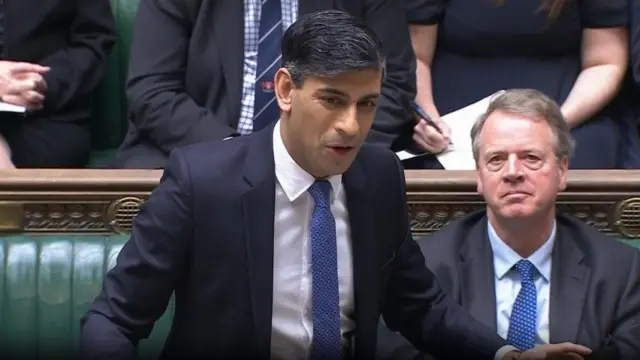 Rishi Sunak stands in the Commons dressed in a blue suit and blue tie