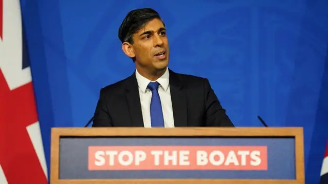 Sunak speaks at a lectern branded with the stop the boats motto