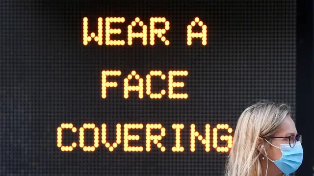 Sign displaying 'wear a face covering' while person wears a mask