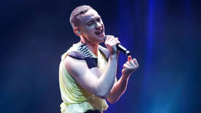 Olly Alexander performs in a yellow tank top with a blue background