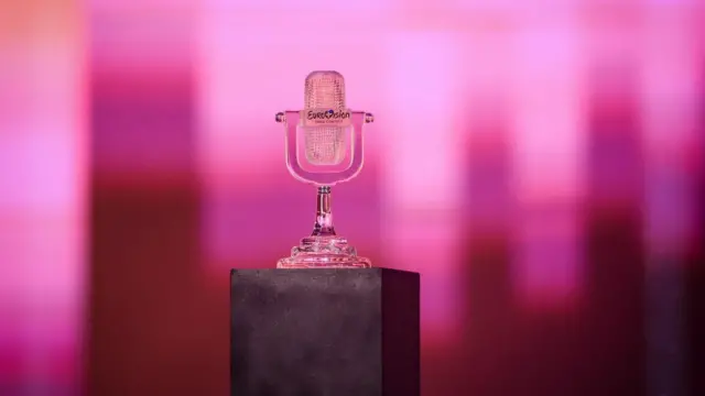 The iconic glass microphone awarded to the winner of the Eurovision Song Contest is seen with a pink screen in the background