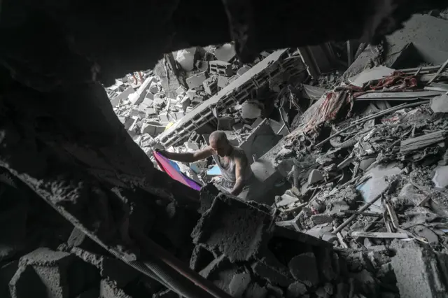 A man, covered with dust, is trying to get hold of some of his possessions from his destroyed family house