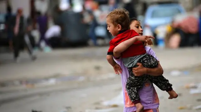 A Palestinian girl carries a toddler as people flee Rafah in the southern Gaza Strip to a safer location