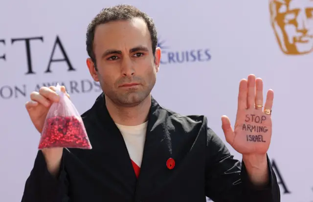 British actor Khalid Abdalla holding up his hand with the message 'stop arming Israel' scrawled on it