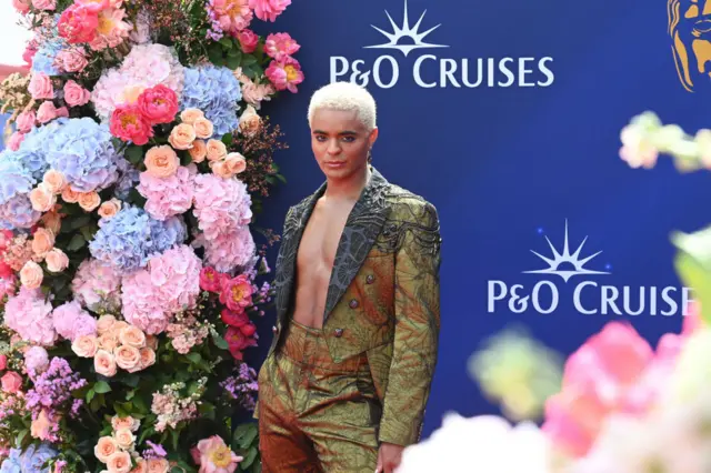 Layton Williams in front of a big bunch of flowers at the Baftas