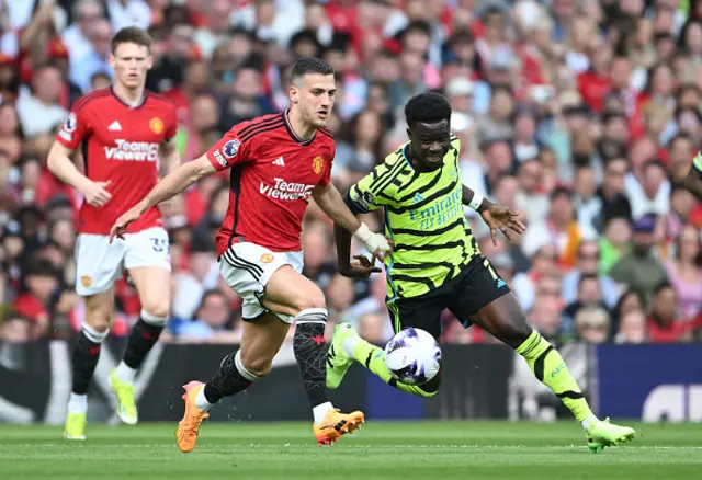 Bukayo Saka of Arsenal chases the loose ball whilst under pressure from Diogo Dalot