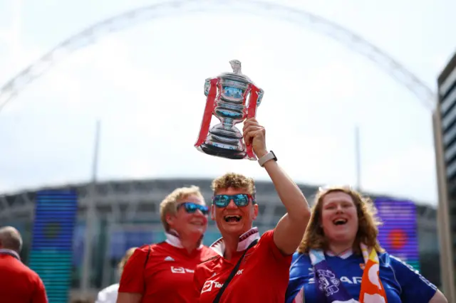 A fan holds aloft a cutout of the FA Cup trophy on Wembley way