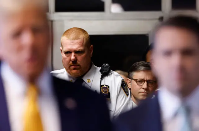 House Speaker Mike Johnson stands behind Donald Trump in the hallways of the New York courthouse