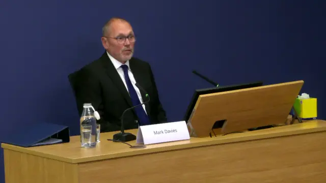 Mark Davies sits in front of a brown desk