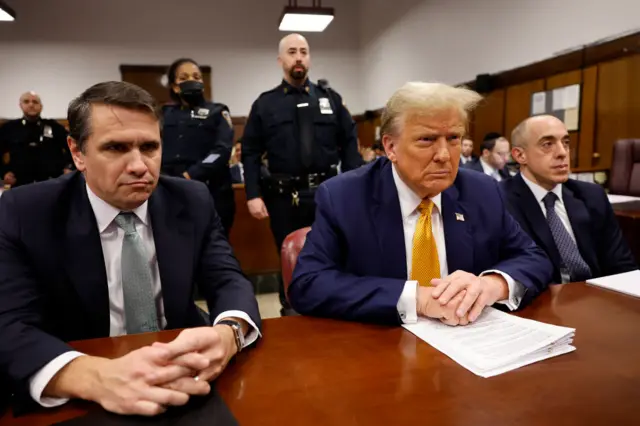 Donald Trump is sitting at the defence table alongside his lawyers.