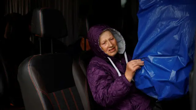 Hanna holds a bird cage covered in a blue plastic bag