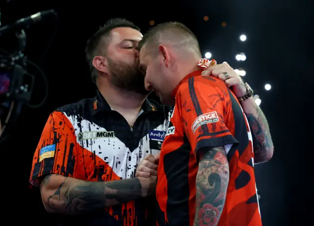 Michael Smith kisses Nathan Aspinall on the head after beating him to reach the Premier League Darts play-offs