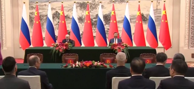 Putin and Xi sitting at a table in front of the media