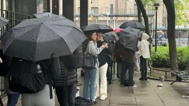 People stand with umbrellas outside a New York court, waiting for Donald Trump's trial