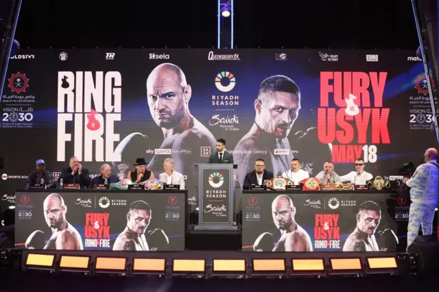 Tyson Fury and Oleksandr Usyk sit at a table with their managers and promoters for a news conference