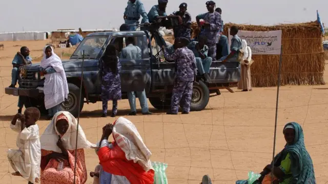 Refugees wait to get into a water station watched by armed police at the Abu Shouk camp near El Fasher in the Darfur region of northern Sudan, Tuesday August 24, 2004