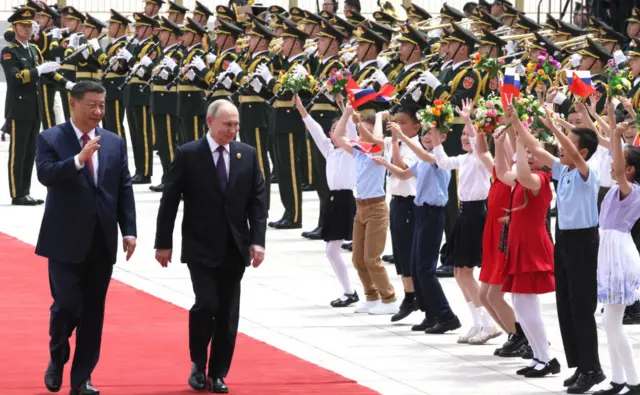 Putin being greeted by a ceremonial guard and received a red-carpet welcome in Beijing on 16 May 2024