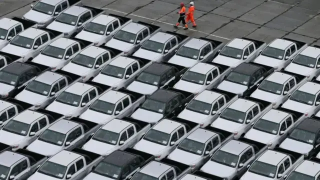 Workers walk past new Chinese cars unloaded from a ship at a commercial port in Vladivostok, Russia