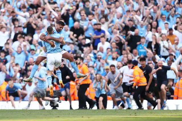 Kyle Walker of Manchester City celebrates victory with teammate Rodri as fans invade the pitch, as Manchester City are named Champions of the Premier League following victory during the Premier League match between Manchester City and West Ham United at Etihad Stadium