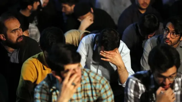 Men seen sat on the floor, some holding their heads, in a street in Tehran, Iran