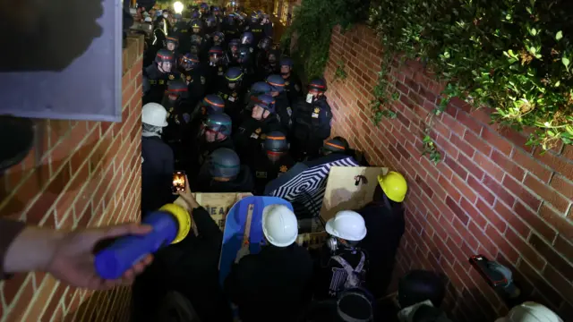 Officers in riot gear try to enter the protest encampment.