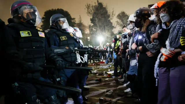 Police in riot gear face off with protesters who are standing opposite them.