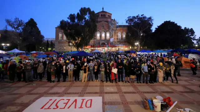 Dozens of protesters and UCLA faculty members standing on the frontlines in the encampment, with a sign that reads "Divest!".