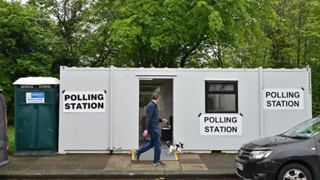 A man walking his dog passes a portable toilet places next to a shipping container used as a polling station