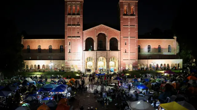 Tents set up outside a UCLA building with protesters holding up a sign that says "No Genocide, End Apartheid".