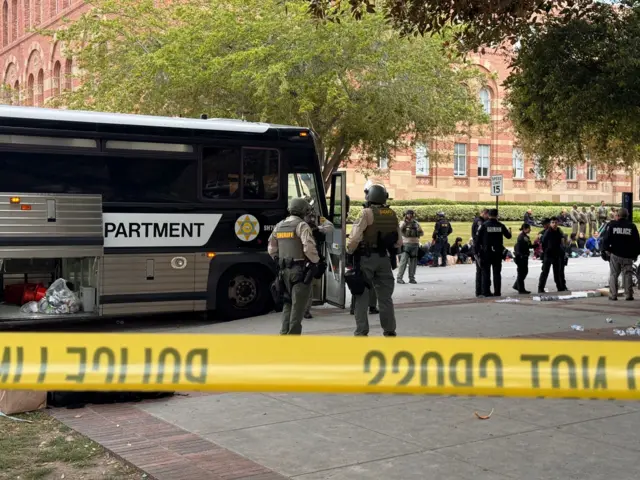 Policemen milling around on the UCLA campus, with police tape visible in the foreground