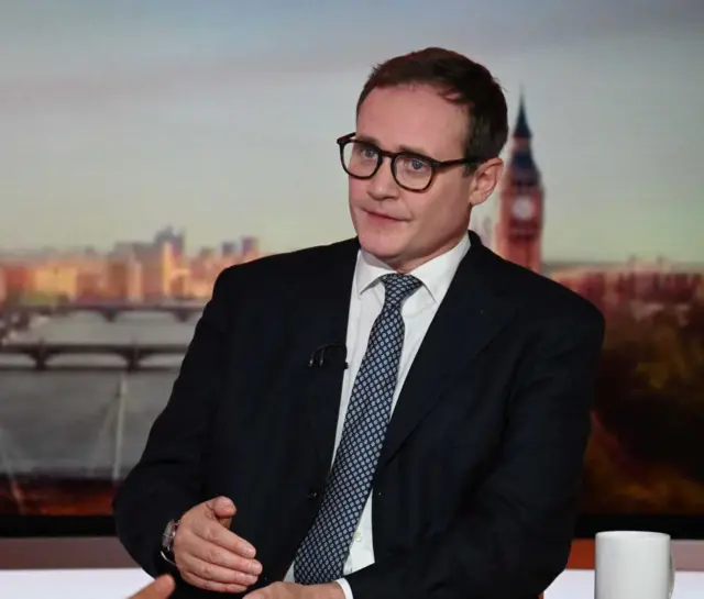 UK Security Minister Tom Tugendhat sitting at a desk with a background image of London during a BBC interview.