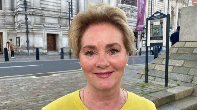 A headshot of Colette Wintle looking at the camera as she stands on steps outside.