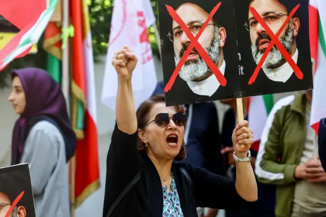 A women holds a poster with the face of Iranian President Ebrahim Raisi crossed out in red, and her other hand up in the air in a fist, at a protest against the Iranian regime, outside the Iranian embassy in Berlin.